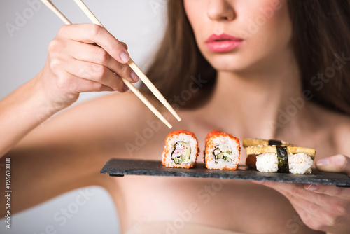 cropped image of sexy naked girl taking sushi with chopsticks