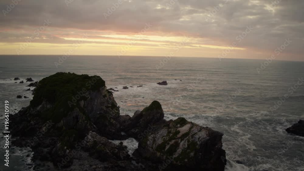 Sunset aerial shot panning over large boulders in the ocean with birds flying. Sunset aerial shot panning over large boulders in the ocean with birds flying.