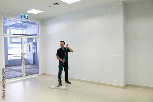 Asian male janitor mopping floor in walkway office building. Commercial Cleaning Services concept.