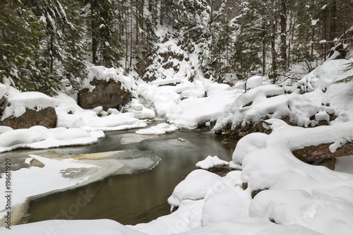 Stunning winter landscape, stones on wintry river covered snow and small waterfall
