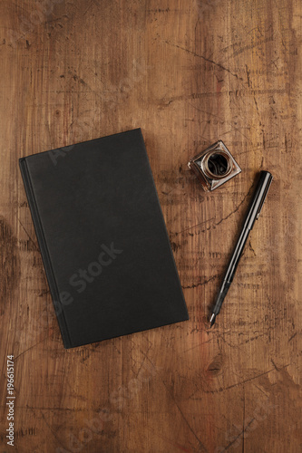 An overhead photo mockup of a black book with a fountain pen, an ink well, and a place for text
