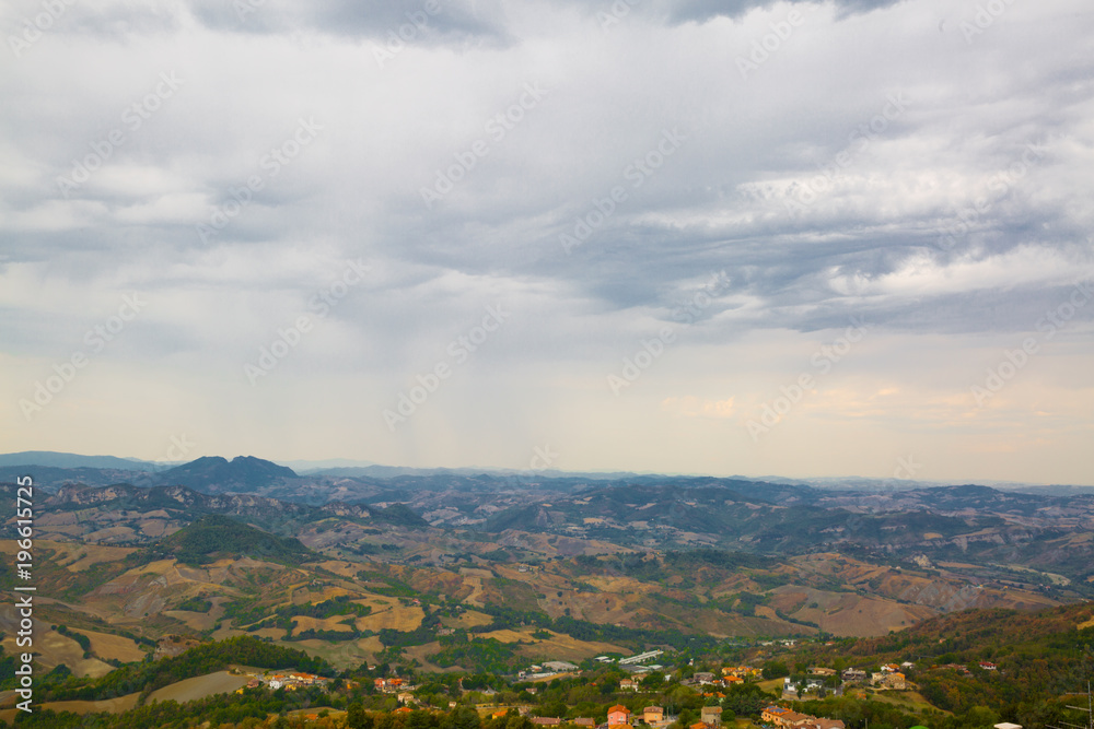 Panoramic view of San Marino. Green valley with orange roofs houses. Cloudly sky in summer.
