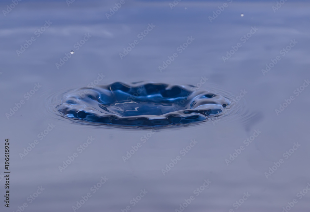 drop of water liquid with splash isolated. the drop explodes in the water sending spray to the sides and circle ripples around it. the water is blue drop of water liquid with splash isolated. the drop explodes in the water sending spray to the sides and circle ripples around it. the water is blue