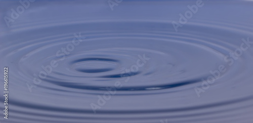 drop of water liquid with splash isolated. the drop explodes in the water sending spray to the sides and circle ripples around it. the water is blue
