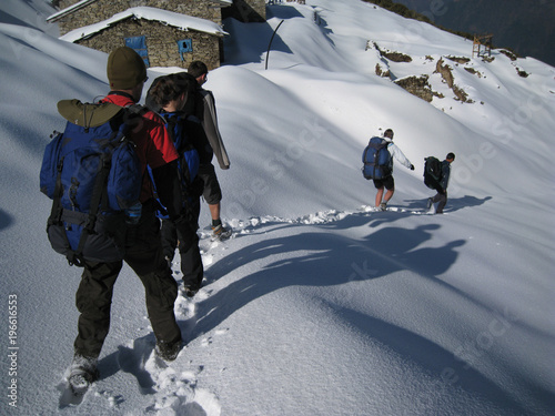 Hikers trekking in the Himalayas cast long shadows in the early morning as they make fresh foot steps in the snow after leaving tea house on Annapurna trail photo