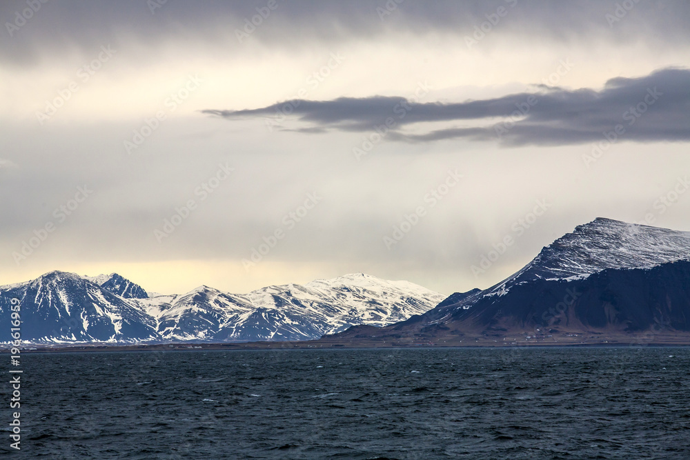 Evening Island coast with the dramatic sky and the snow mountain in the background