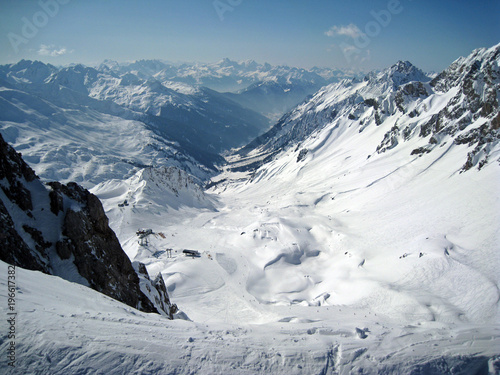 Vertigo inducing view taken from a snowy cliff edge on a crystal clear day in St Anton in the Austrian Alps, of a very steep, deep, and wide snow covered valley
