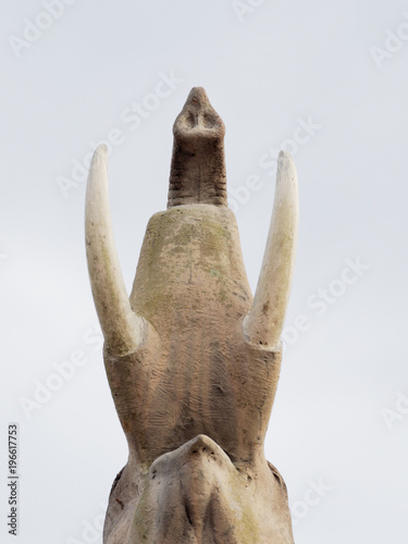 Ant eye view of elephant statue show the lower parts of neck, tusks, and trunk over pale blue sky background