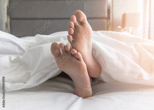 World sleep day, sleeping comfort relaxation and bedtime insomnia concept with young girl’s bare lazy foot laying on bed resting in comfy hotel bedroom on white bed sheet