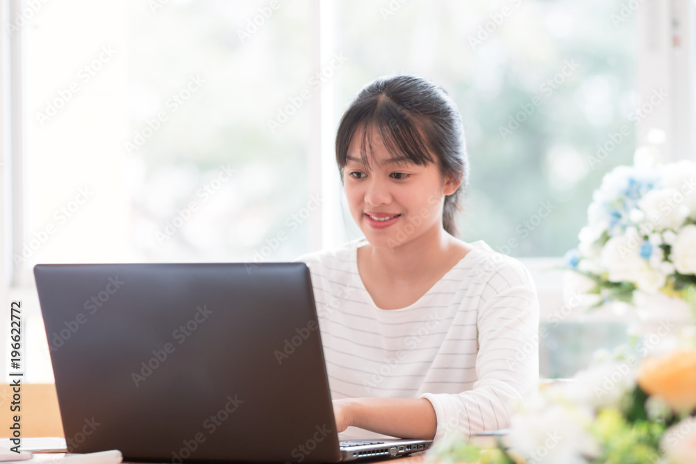 Online searching social networks by Smartphone Concept: Asian Cute Woman using black laptop computer for shopping or typing sms message to her customer in offices with flower background Online searching social networks by Smartphone Concept: Asian Cute Woman using black laptop computer for shopping or typing sms message to her customer in offices with flower background