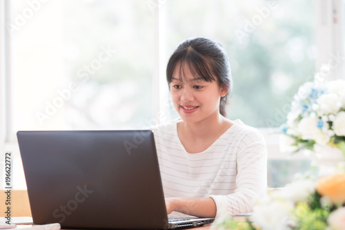 Online searching social networks by Smartphone Concept: Asian Cute Woman using black laptop computer for shopping or typing sms message to her customer in offices with flower background