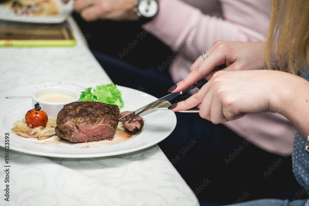 woman cuts a piece of fresh grilled bbq roast beef steaksoup sauce small jug glass served on a table in a restaurant