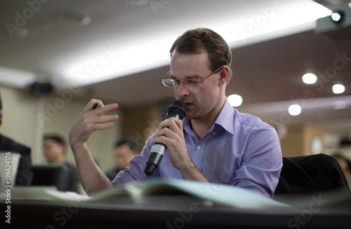 Professional Man Speaks During Presentation While Sitting Behind Desk