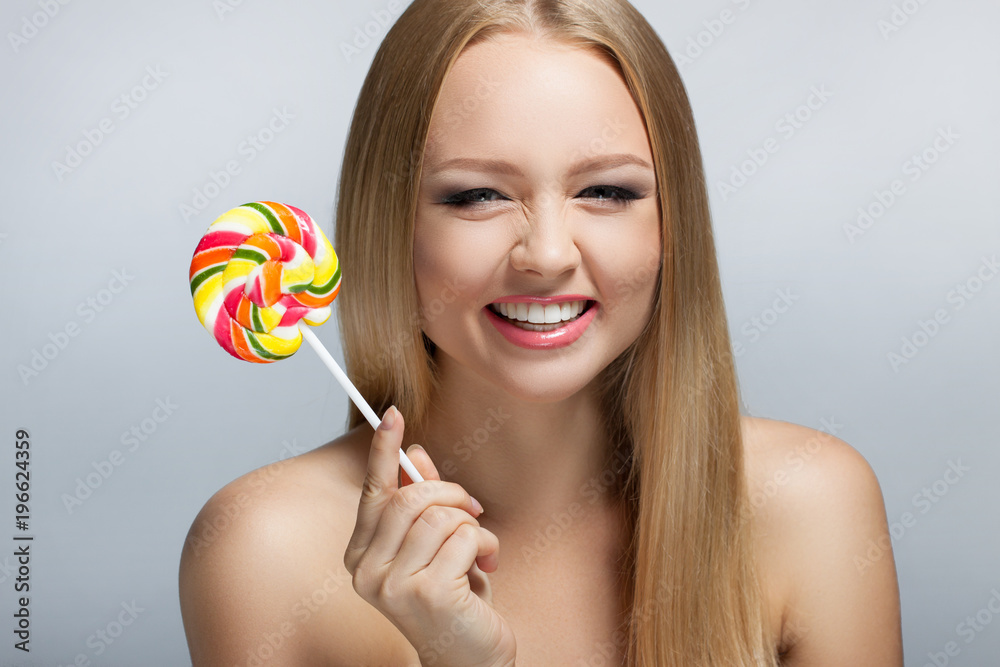 Cute young woman looking into the camera and holding a lollipop. Positive human emotions. Laugh