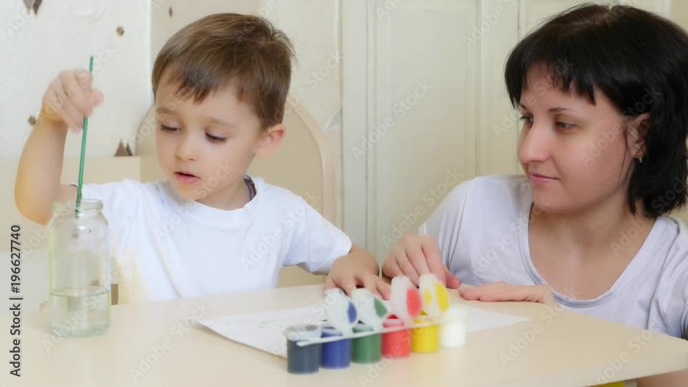 The child and mother paint with watercolor on a white sheet of paper. The child and mother paint with watercolor on a white sheet of paper.