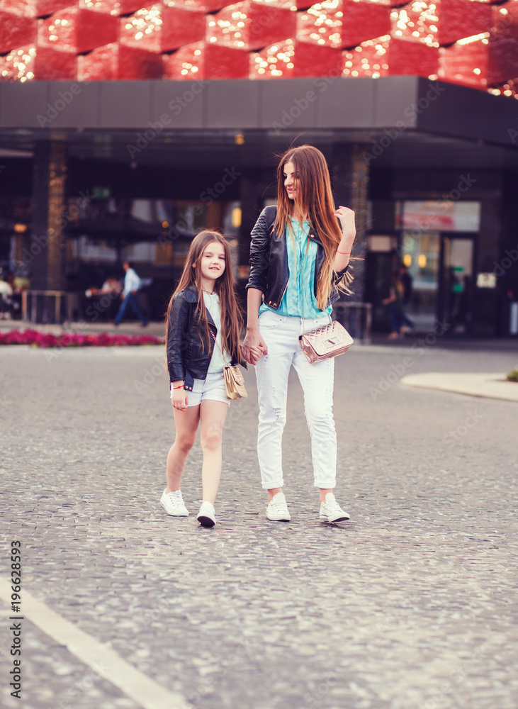 Mother and little daughter walking together in city