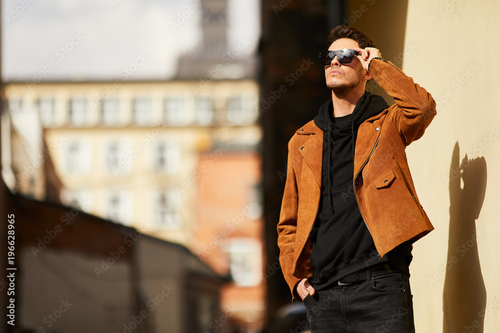 Model looking man stand near the wall and hold his glasses towards the sun shine Model looking man stand near the wall and hold his glasses towards the sun shine
