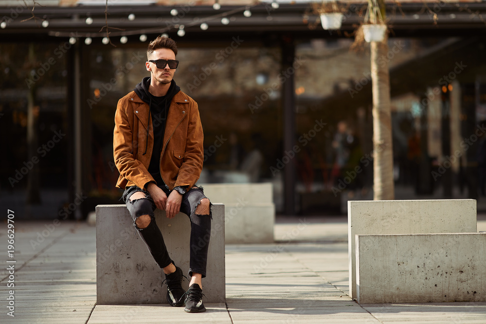 Fototapeta premium Model looking man sit on the bench in modern park background, look on his watch and around