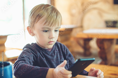 Cute little boy playing games on smartphone at home.