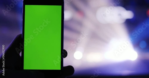 closeup view of modern smartphone on blurred colorful cocert lighting background / man hand holding mobile green screen chromakey mock-up photo camera night club music clubbing app stream chat wifi photo