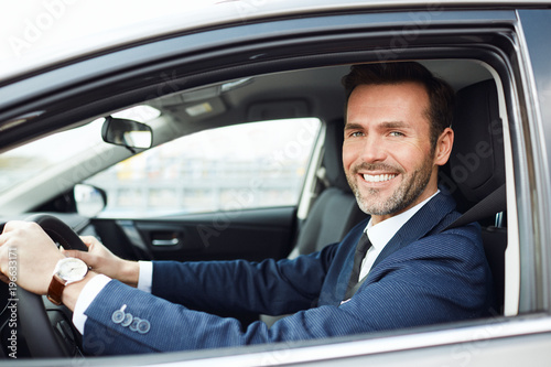 Smiling businessman driving car and looking at camera