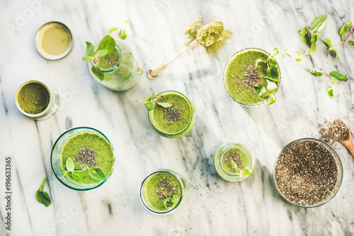 Matcha green vegan smoothie with chia seeds and fresh mint in glasses and bottles over marble background, top view. Clean eating, detox, alkaline diet, weight loss food concept photo