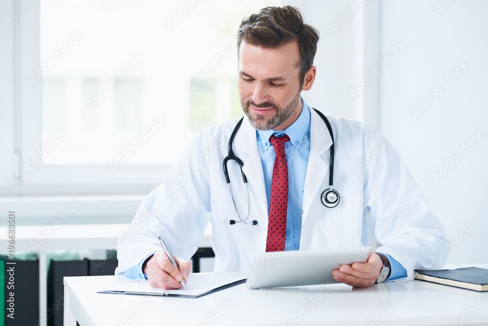 Male doctor sitting in office writing medical documents Male doctor sitting in office writing medical documents