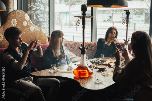 A young company of people is smoking a hookah and communicating in an oriental restaurant. Lebanon cuisine served in restaurant. Traditional meze lunch