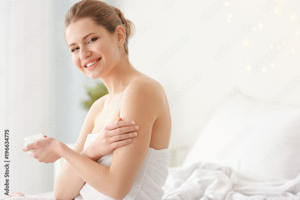 Young woman applying cream onto her skin indoors Young woman applying cream onto her skin indoors