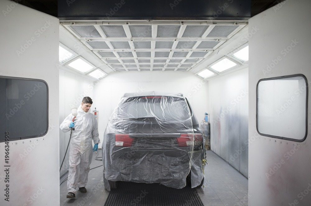 Auto painter painting a car inside a paint booth Auto painter painting a car inside a paint booth