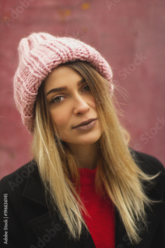 blonde girl with big eyes and plump lips against a pink background. woman in voluminous warm-colored powder hat.