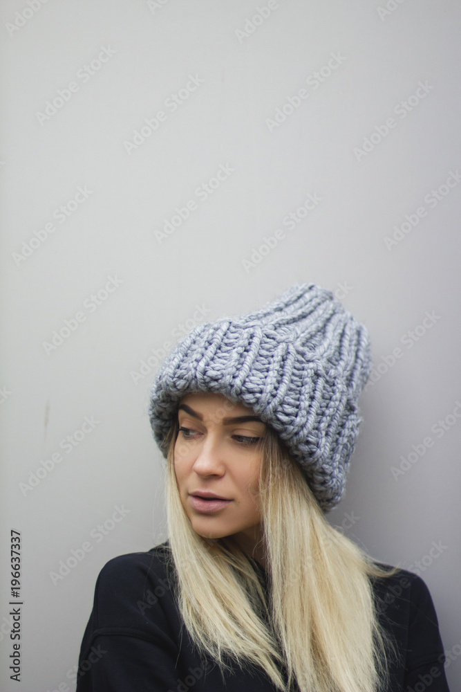 blonde girl with big eyes and plump lips against a light gray background. woman in a voluminous warm gray hat. blonde girl with big eyes and plump lips against a light gray background. woman in a voluminous warm gray hat.