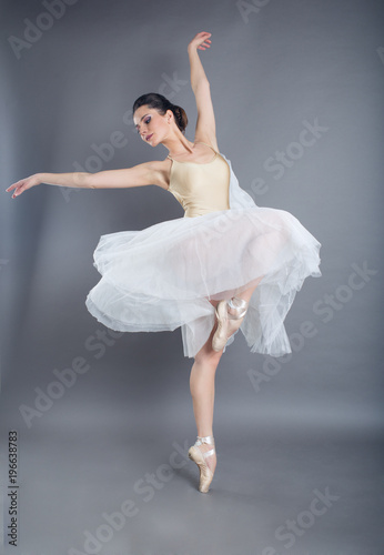 Beautiful slim woman ballet dancer in studio isolated on gray