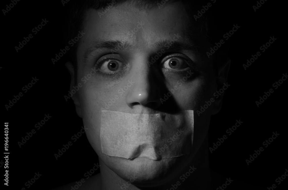 Face of a frightened man with a mouth taped violently with his mouth isolated on a black background Face of a frightened man with a mouth taped violently with his mouth isolated on a black background