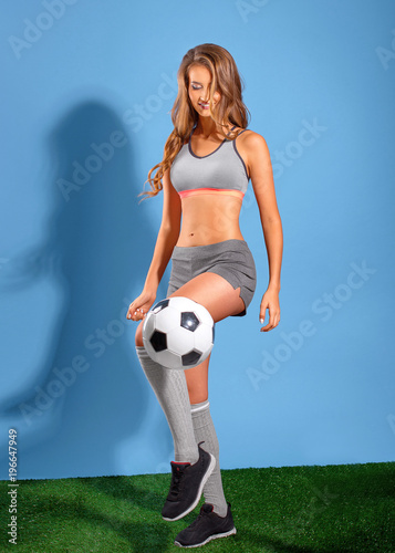 Beautiful sports girl posing with a ball as a football player on a blue background