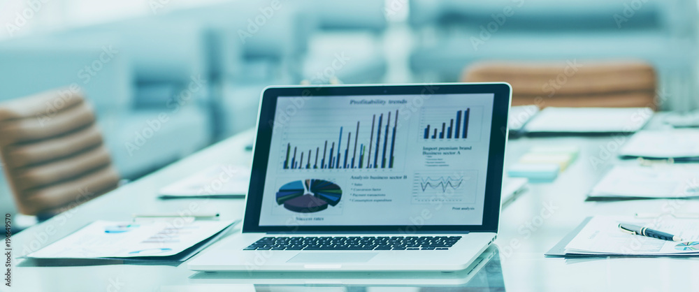 workplace with open laptop and financial documents prepared for meeting business partners