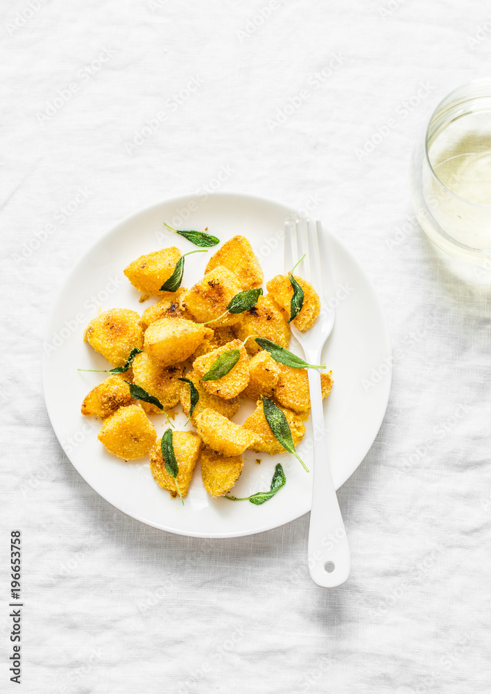 Crispy polenta crust potatoes baked with sage butter and a glass of white wine on a light background, top view Crispy polenta crust potatoes baked with sage butter and a glass of white wine on a light background, top view