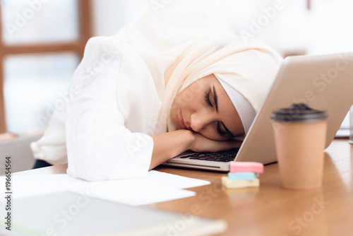 Arab woman wearing a headscarf sitting tired at work.
