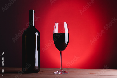 bottle of wine and glass with red wine, on red background, copy space