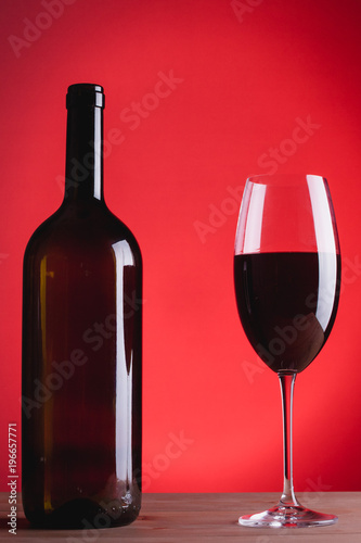 bottle of wine and glass with red wine, on red background, copy space