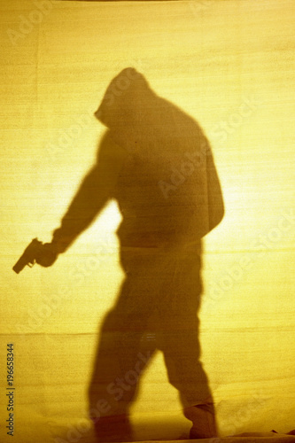 The shadow behind fabric of a man with a gun.