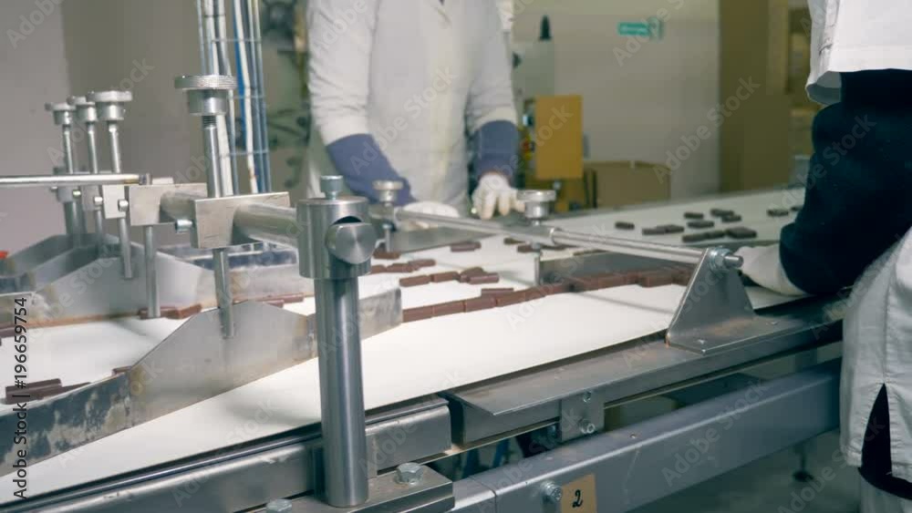 Chocolate candies are moving along the conveyor and then are being sorted by workers