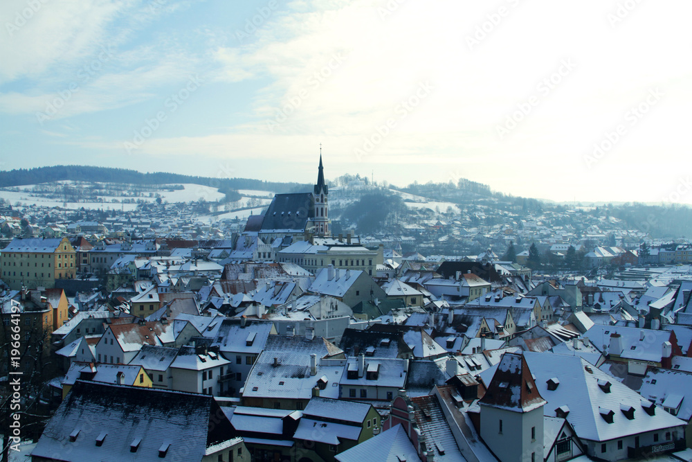 Beautiful and historical town of Český Krumlov in the South Bohemian Region of the Czech Republic portraying its picturesque architecture, snowy rooftops and an old church during one winter afternoon