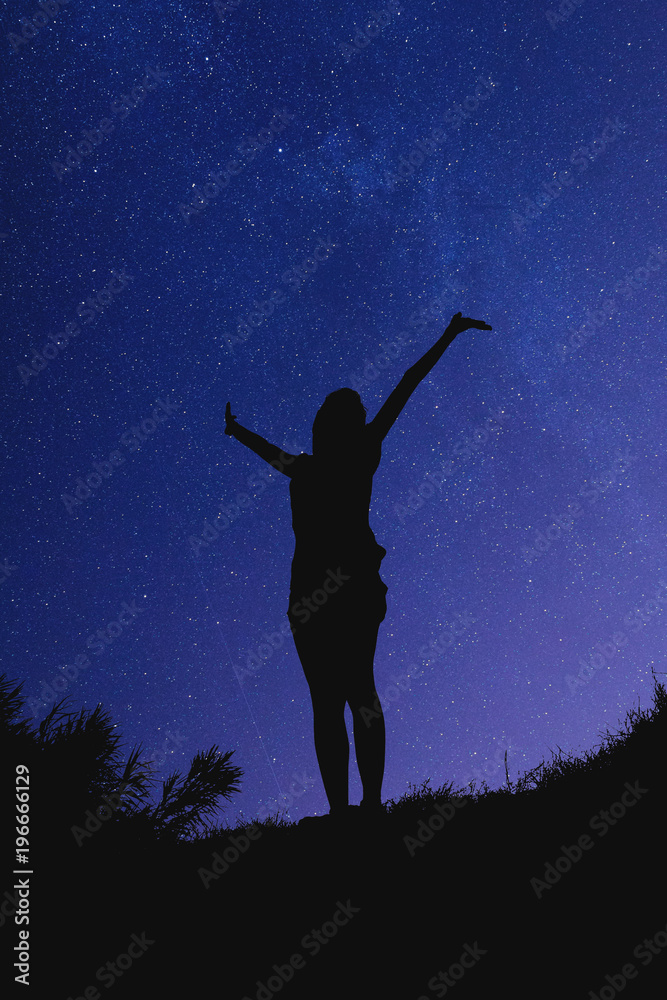 Silhouette of a girl with hands in the air at night.