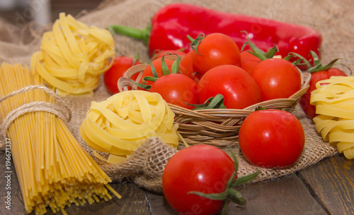 Long and twisted pasta with cherry tomatoes on a brown wooden table on a beige bag