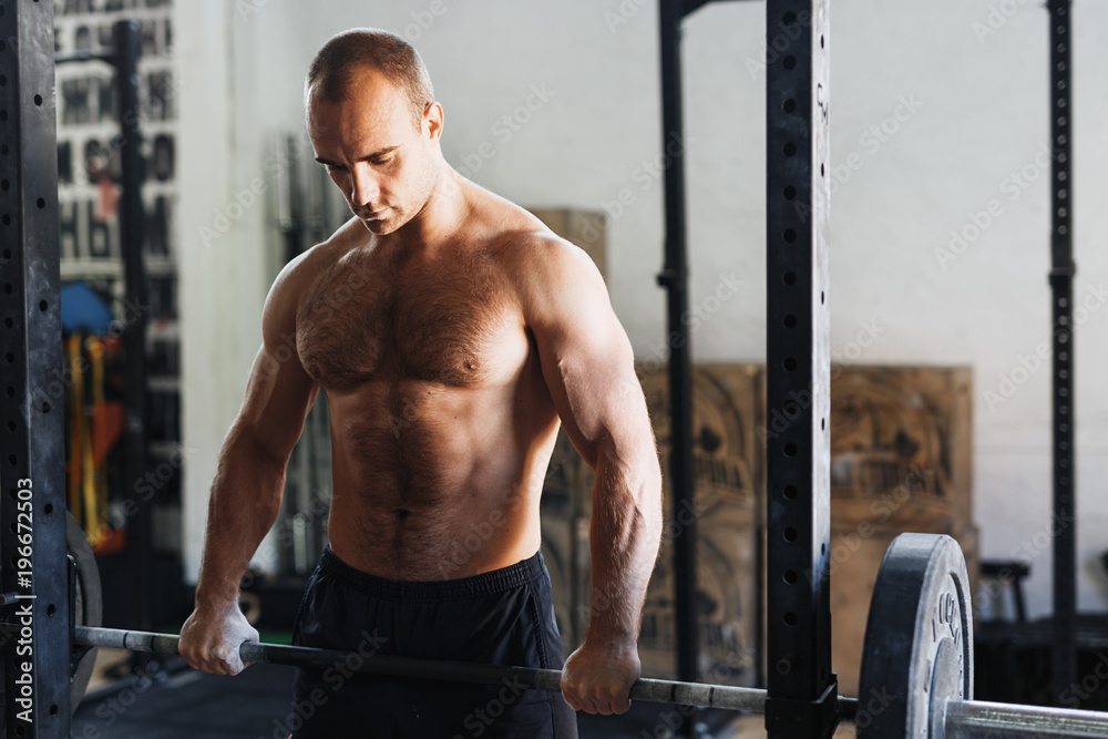 Young athlete taking rest after training in gym, holding a barbell Young athlete taking rest after training in gym, holding a barbell