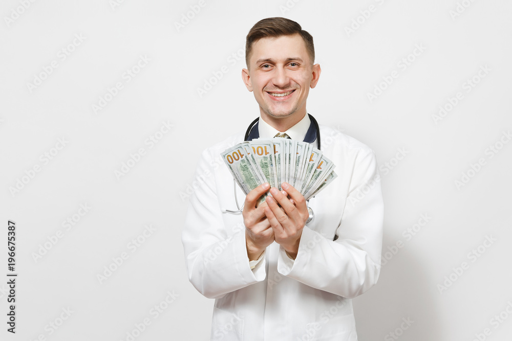 Smiling young doctor man isolated on white background. Male doctor in medical uniform, stethoscope holding bundle of dollars, banknotes, cash money. Healthcare personnel, health, medicine concept. Smiling young doctor man isolated on white background. Male doctor in medical uniform, stethoscope holding bundle of dollars, banknotes, cash money. Healthcare personnel, health, medicine concept.