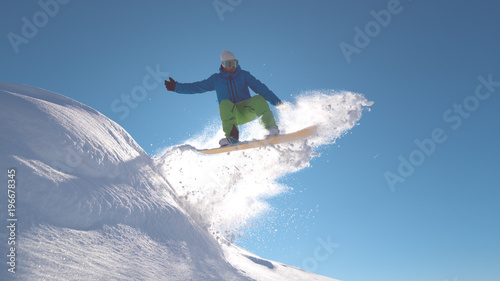 CLOSE UP: Pro snowboarder jumping in fresh snow, spraying snowflakes over sun