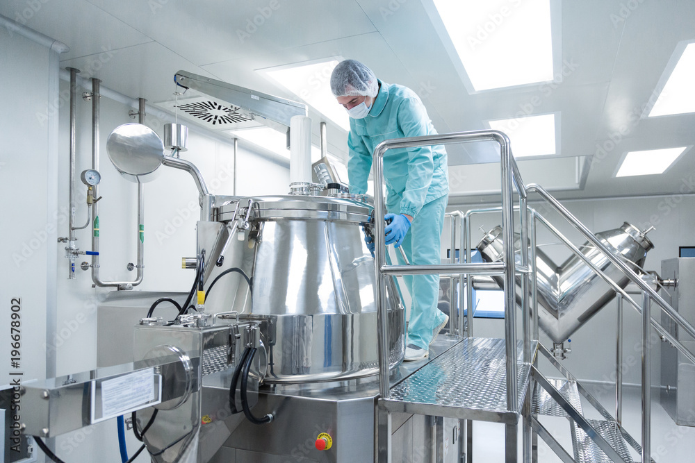 Pharmaceutical factory man worker in protective clothing operate production line in sterile working conditions