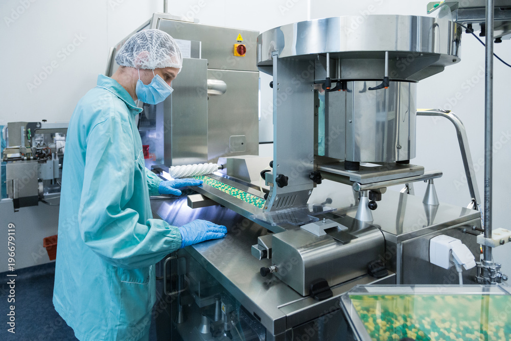 Pharmaceutical industry man worker in protective clothing operating production of tablets in sterile working conditions Pharmaceutical industry man worker in protective clothing operating production of tablets in sterile working conditions